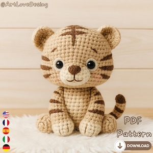 Puede incluir: Un juguete de tigre tejido a ganchillo en beige y marrón. El tigre tiene rayas marrones oscuras, una nariz marrón y ojos negros grandes. El texto "PDF Pattern" y "Download" es visible. El juguete está sobre una superficie blanca y esponjosa.