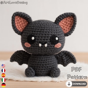Könnte beinhalten: Eine gehäkelte Fledermaus mit dunkelgrauem Körper, rosa Innenohren und kleinen weißen Zähnen. Die Fledermaus hat schwarze Augen mit weißen Glanzlichtern und kleine Flügel. Der Text "PDF Pattern" ist enthalten.