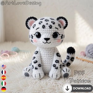 Peut inclure: Un léopard blanc crocheté avec des taches noires, de grands yeux noirs et des joues roses. La peluche faite à la main a une queue et des oreilles noires et blanches. L'image comprend le texte "PDF Pattern" et une icône de téléchargement.
