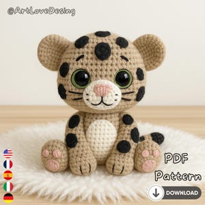 Peut inclure: Un bébé léopard crocheté avec des taches noires, de grands yeux verts et un nez rose. La peluche faite à la main est beige et blanche, avec une petite queue et des pattes. L'image comprend le texte "PDF Pattern" et une flèche de téléchargement.