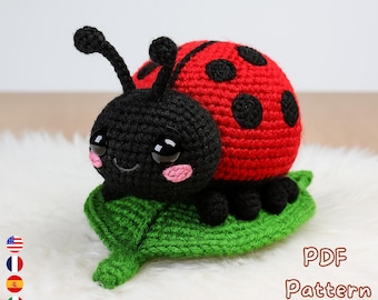 May include: A crocheted ladybug with a red shell and black spots, black head, and a green leaf base. The ladybug has large, expressive eyes and pink cheeks. The image includes the text "PDF Pattern Download".