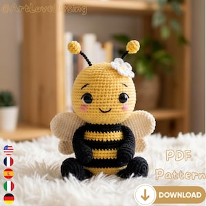 Può includere: Una bambola a forma di ape all'uncinetto con corpo giallo, strisce nere e ali color crema. L'ape ha un viso sorridente, guance rosa e un fiore bianco sulla testa. L'immagine include il testo "PDF Pattern" e un pulsante di download.
