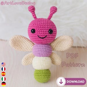 Può includere: Un giocattolo a farfalla all'uncinetto fatto a mano nei toni del rosa, viola, crema e verde. Il giocattolo ha grandi occhi neri e una bocca sorridente. Le ali sono color crema e il corpo è fatto di sfere impilate. Il testo "PDF Pattern" è incluso.