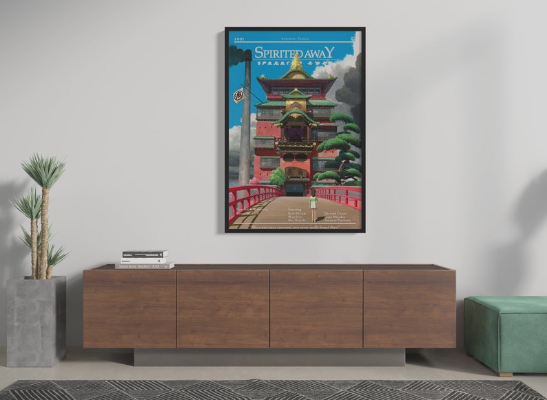May include: A framed poster with a minimalist design featuring a red and gold building with a bridge leading to it. The poster is titled "Spirited Away" and includes the film's credits.