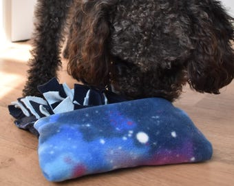 May include: A rectangular fabric snuffle mat featuring a vibrant galaxy print with shades of blue, purple, and white stars. The mat includes multiple layers of dark blue and light blue fabric strips attached to the base for hiding treats.