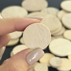 May include: A collection of small, circular, unfinished wooden discs with a light beige color and visible natural wood grain patterns. Each disc is flat and smooth, featuring a simple round shape suitable for various craft projects.