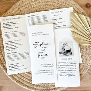 Op de afbeelding: Huwelijksceremonieprogramma met zwarte tekst op wit papier. Het programma bevat de volgorde van de gebeurtenissen, de namen van de bruid en de bruidegom, en een foto van het paar. De tekst bevat "Welkom bij de huwelijksmis ter ere van Stephanie Marie en Tanner Reid".