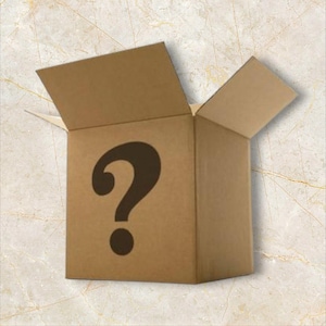 May include: A brown cardboard box with the top flaps open, revealing the inside. A large black question mark is printed on the front of the box. The box is on a light-coloured surface.