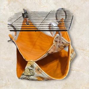 May include: Orange and floral patterned pet hammock. The hammock is designed to hang inside a cage. The interior is a solid orange color, while the exterior features a white fabric with a floral and leaf pattern.