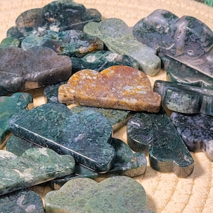 May include: A collection of green, brown, and white agate stones carved into cloud shapes. The stones are smooth and polished, and they have a variety of patterns and textures.