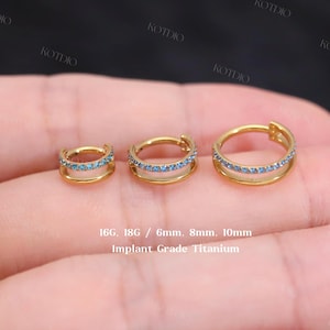 Pode incluir: Três brincos de argola dourados com pedras preciosas azuis, em vários tamanhos. Os brincos são feitos de titânio de grau de implante. O texto na imagem indica os tamanhos: 16G, 18G, 6mm, 8mm e 10mm.