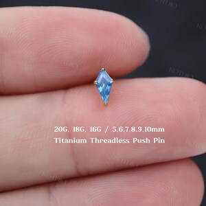 May include: A small, gold-colored titanium threadless push pin with a light blue, kite-shaped gem. The image includes text indicating sizes 20G, 18G, and 16G, and gem sizes 5.6, 7, 8, 9, and 10mm.