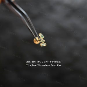 May include: A gold-toned titanium threadless push pin body jewelry featuring three rectangular green moss agate stones arranged in a staggered vertical cluster. The text 20G, 18G, 16G / 5.6.7.8.9.10mm Titanium Threadless Push Pin is visible.