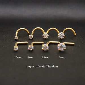 May include: A set of six gold nose rings with clear gemstones. The rings are available in sizes 1.5mm, 2mm, 2.5mm, and 3mm. The text "Implant Grade Titanium" is printed below the rings.