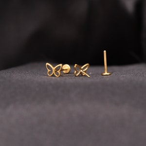 May include: A pair of gold butterfly earrings with a post and butterfly back. The earrings are on a black background.