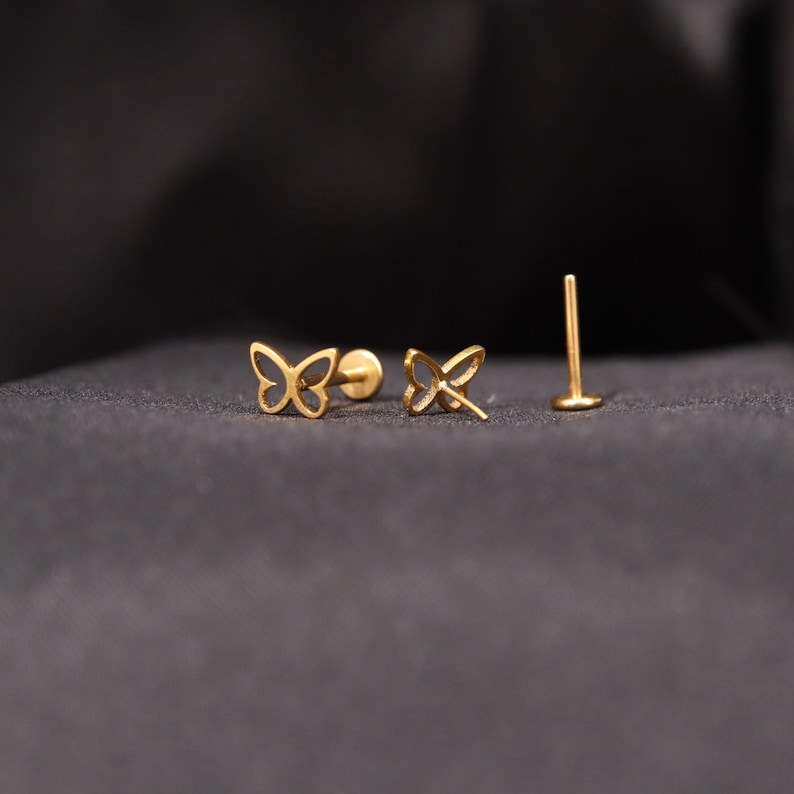 May include: A pair of gold butterfly earrings with a post and butterfly back. The earrings are on a black background.