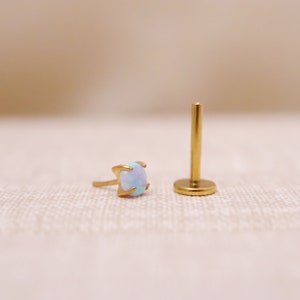 May include: A gold-toned opal gemstone earring with a prong setting. The earring is shown next to a gold-toned post.