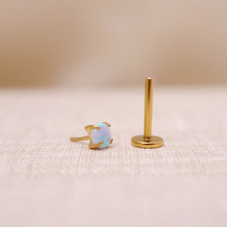 May include: A gold-toned opal gemstone earring with a prong setting. The earring is shown next to a gold-toned post.