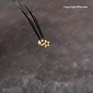 Op de afbeelding: Een gouden sterbedel met een kleine gouden kraal aan een zwart koord.