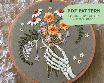 May include: Embroidered hoop art featuring a skeletal hand holding a bouquet of colorful flowers. The flowers are a mix of orange, pink, and blue. There is a spider web and a spider in the lower left corner. The text "PDF PATTERN EMBROIDERY PATTERN + STITCH GUIDE" is in the upper right corner.