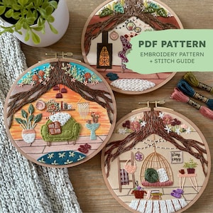 May include: Three embroidery hoop art pieces with a nature theme. Each hoop features a different scene with a tree, a cosy living room, and a birdcage. The hoops are on a wooden surface with embroidery floss.