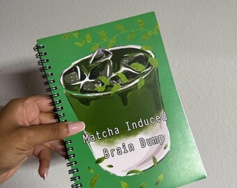 Może przedstawiać: Zielony notatnik w spiralę z ilustracją napoju matcha i napisem "Matcha Induced Brain Dump". Notatnik jest trzymany na jasnym tle. Projekt zawiera zielone liście.