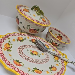 May include: A white ceramic serving platter with a yellow rope border and red and white floral design. The platter features a pumpkin motif and comes with a matching serving bowl and lid.