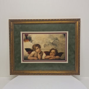May include: Framed print of a painting depicting two cherubs with wings, one looking to the side and the other looking at the viewer. The cherubs are painted in a realistic style with soft, muted colours.