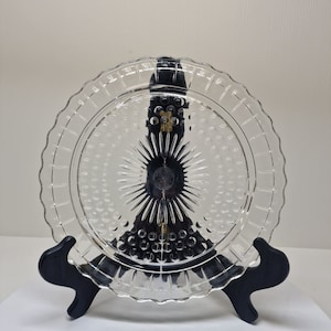 May include: A clear glass plate with a raised, textured design. The plate has a scalloped edge and a central starburst pattern.