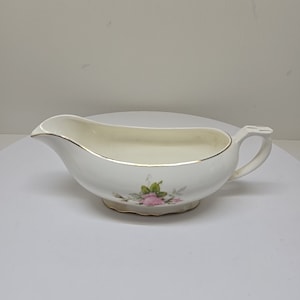 Puede incluir: Salsera de porcelana blanca con un diseño de rosa rosa y un borde dorado.