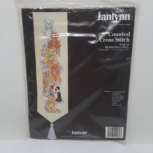 May include: A counted cross stitch pattern featuring a stack of teddy bears with a bell pull at the bottom. The pattern is called "Bears Bell Pull" and is numbered #125-74. The finished size is 58.7 cm by 13.97 cm.