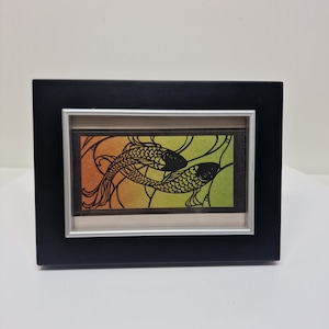 May include: A framed black and white silhouette of two fish swimming in a gradient background of orange, yellow, and green.