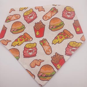 May include: A cream-colored bandana featuring a repeating pattern of cartoon fast food items. The design includes burgers, fries, pizza slices, chicken wings, and wraps. Red and yellow are the dominant colors in the food illustrations.