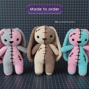Könnte beinhalten: Drei handgefertigte Häkelhasen-Puppen. Jeder Hase ist in der Mitte mit zwei verschiedenen Farben geteilt. Die Hasen haben lange Ohren, gestickte Details und schwarze Knopfaugen. Der Text "Made to order" steht über den Hasen.