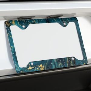 May include: A teal and gold marble patterned license plate frame with a white background. The frame is attached to the back of a silver car.