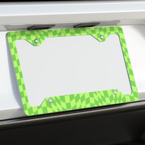 May include: A white car with a green and white checkered license plate frame. The car has dual exhaust pipes.