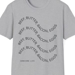 May include: A heather gray crew neck t-shirt with the words "BEEF, BUTTER, BACON, EGGS" in a wavy pattern. The text "CARNIVORE LIFE" is printed below the wavy text.