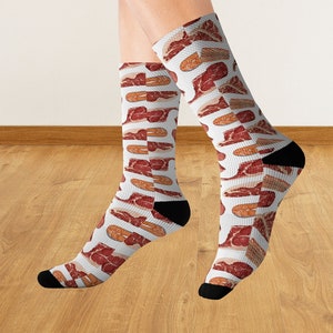 May include: A pair of white socks with a repeating pattern of red and brown steak slices. The socks are worn on a person's feet.