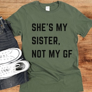 May include: A green t-shirt with the text "She's my sister, not my GF" printed in black.