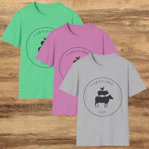 May include: Three t-shirts in different colors: green, pink, and gray. Each shirt features a black and white graphic of a cow, pig, and chicken with the text "CARNIVORE LIFE" in a circle.