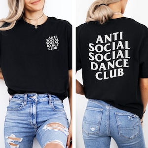 May include: Black t-shirt with the text "ANTI SOCIAL SOCIAL DANCE CLUB" printed in white on the front and back. The shirt is a crew neck and has short sleeves. The model is wearing blue jeans.