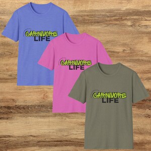 May include: Three t-shirts in different colors with the text "CARNIVORE LIFE" in a graffiti style font. The shirts are light blue, pink, and gray.