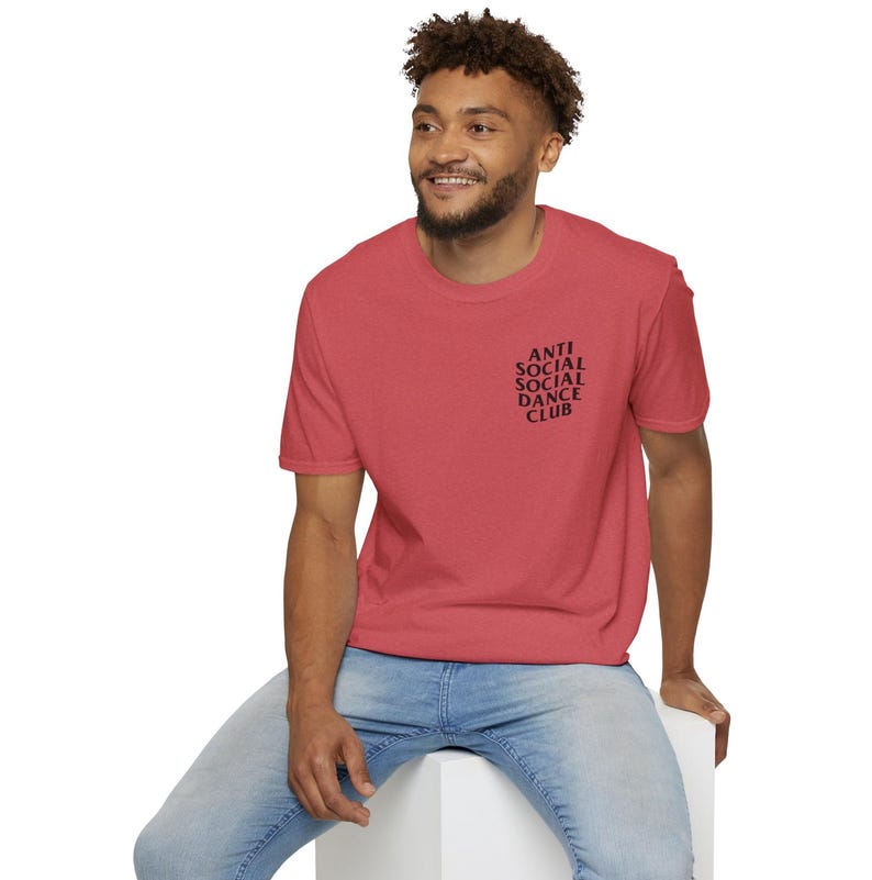 May include: A red t-shirt with the text "ANTI SOCIAL SOCIAL DANCE CLUB" printed in black on the upper left chest. The shirt is short-sleeved and has a crew neck.