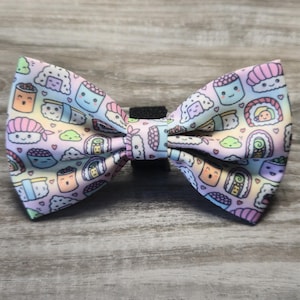 May include: A colorful bow tie featuring a repeating pattern of cute sushi characters on a pastel rainbow background. The bow tie has a black adjustable strap for easy wear.