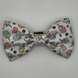 May include: White bow tie with a pattern of colorful cupcakes and paw prints.