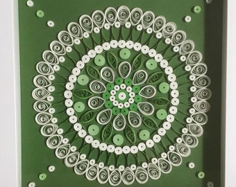 May include: A framed green and white paper quilling mandala art piece. The mandala is made of paper rolls and is surrounded by a white frame.