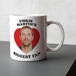 May include: White ceramic mug with a red heart featuring a photo of Chris Martin. The text "Chris Martin's Biggest Fan" is printed on the mug.