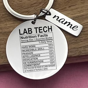 May include: A silver-colored keychain with a round pendant that reads "LAB TECH" and "Nutrition Facts." The pendant lists qualities like "Hard Work" and "Incredible Skill." A smaller tag reads "name."