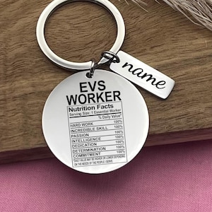 May include: A silver keychain with a round tag that reads "EVS WORKER Nutrition Facts Serving Size: 1 Essential Worker % Daily Value HARD WORK 100% INCREDIBLE SKILL 100% PASSION 100% INTELLIGENCE 100% DEDICATION 100% DETERMINATION 100% COMMITMENT 100% DAILY VALUE MAY BE HIGHER OR LOWER DEPENDING ON THE NEEDS OF THE PEOPLE I SERVE". The tag is attached to a silver ring with a smaller tag that reads "name".