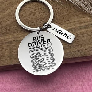 May include: Silver keychain with a round tag that says "Bus Driver Nutrition Facts" and lists qualities like "Hard Work", "Incredible Skill", and "Passion" with a percentage of 100% for each. A smaller tag hangs below with the word "name" on it.